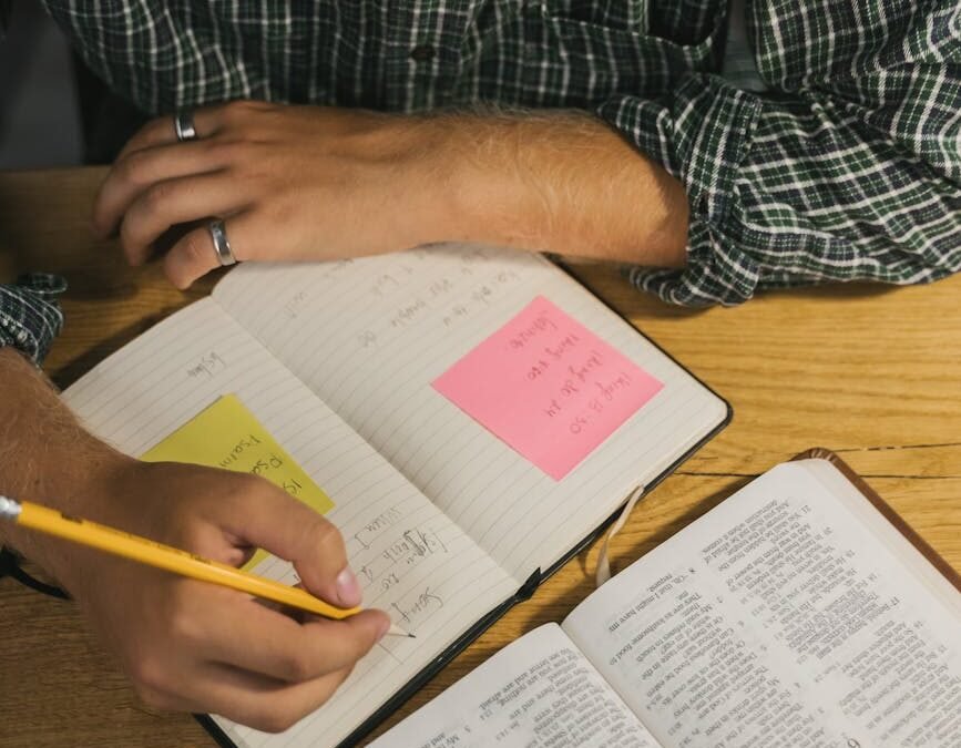 a man writing on a notebook while reading a bible