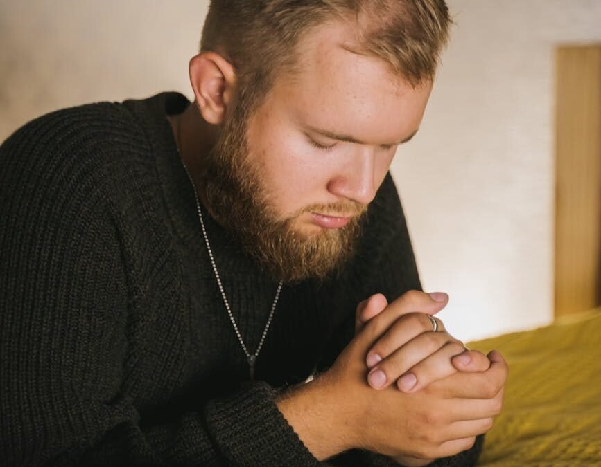 close up shot of a bearded man in black knitted sweater praying