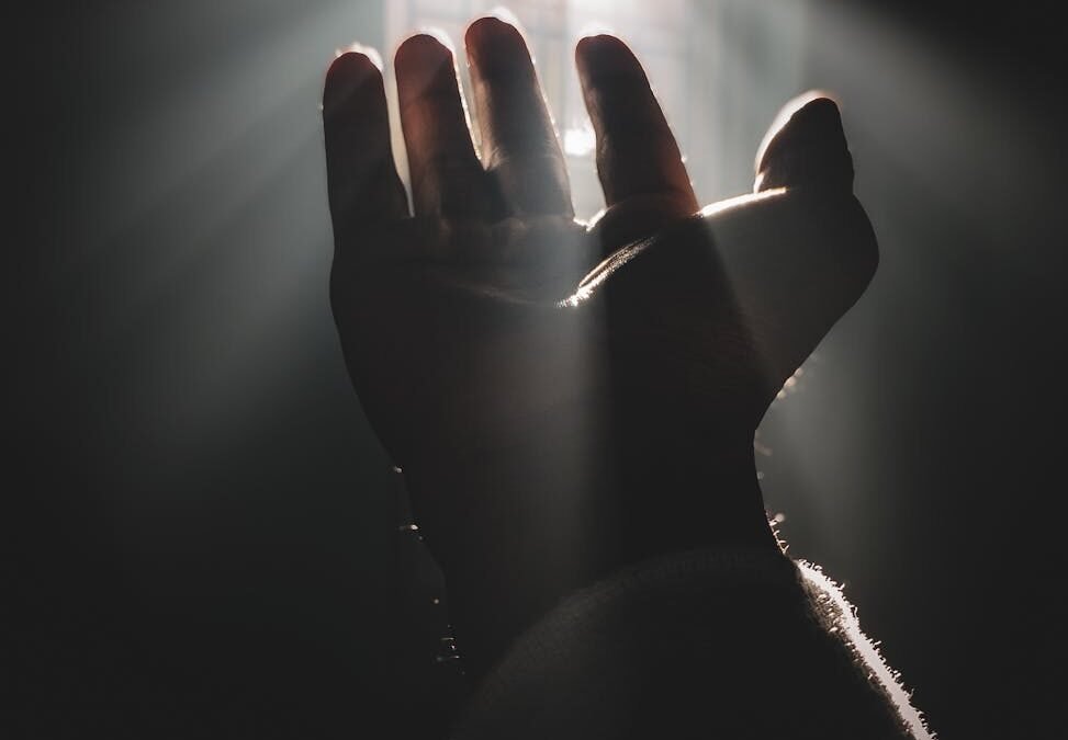 silhouette of a hand reaching for sunlight through window