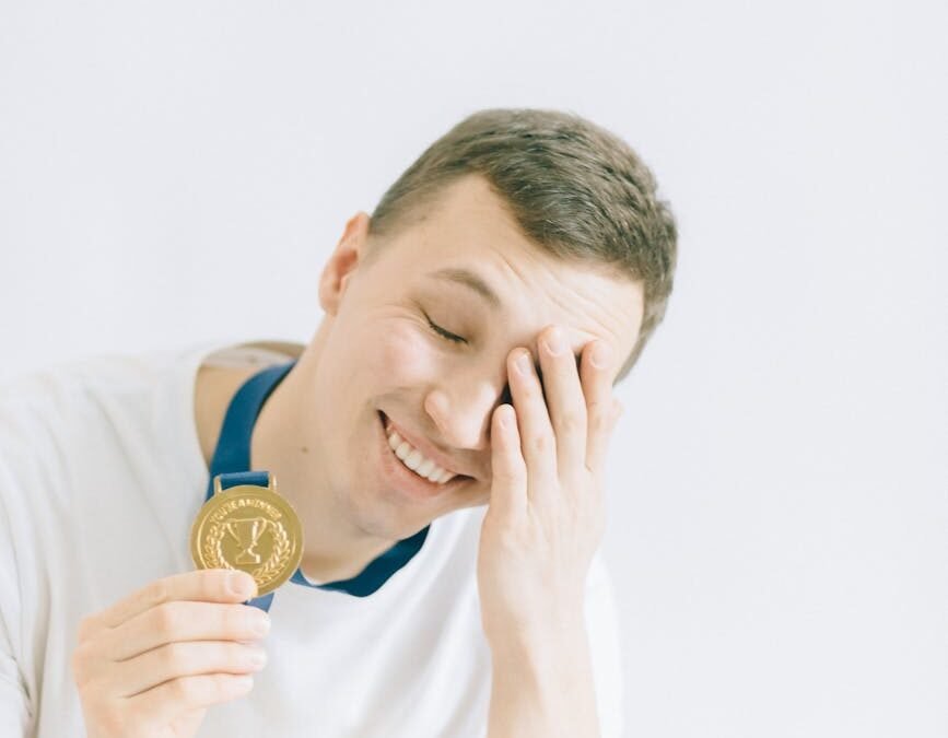 young man in white crew neck t shirt holding a gold medal