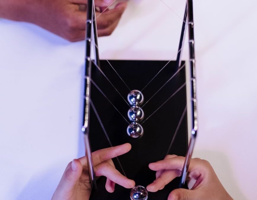 unrecognizable hands of two young people playing metal balls of newtons cradle