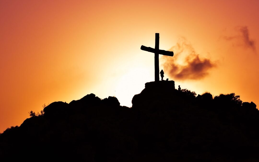 human standing beside crucifix statue on mountain