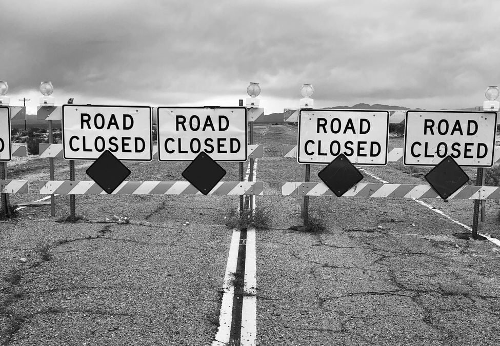 black and white photo of road with road closed signs