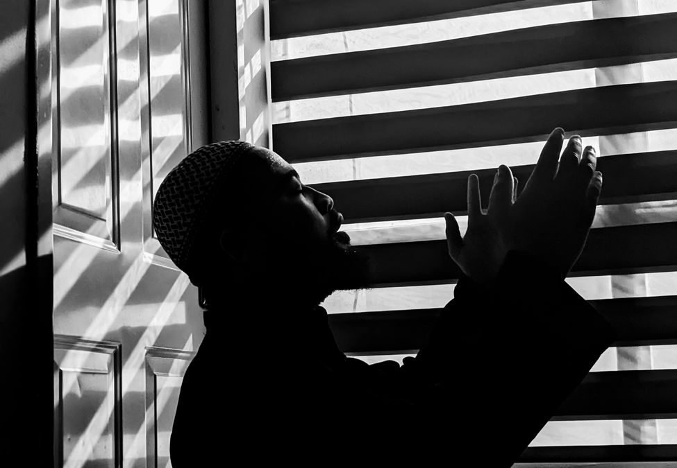 man praying in front of a blinded window