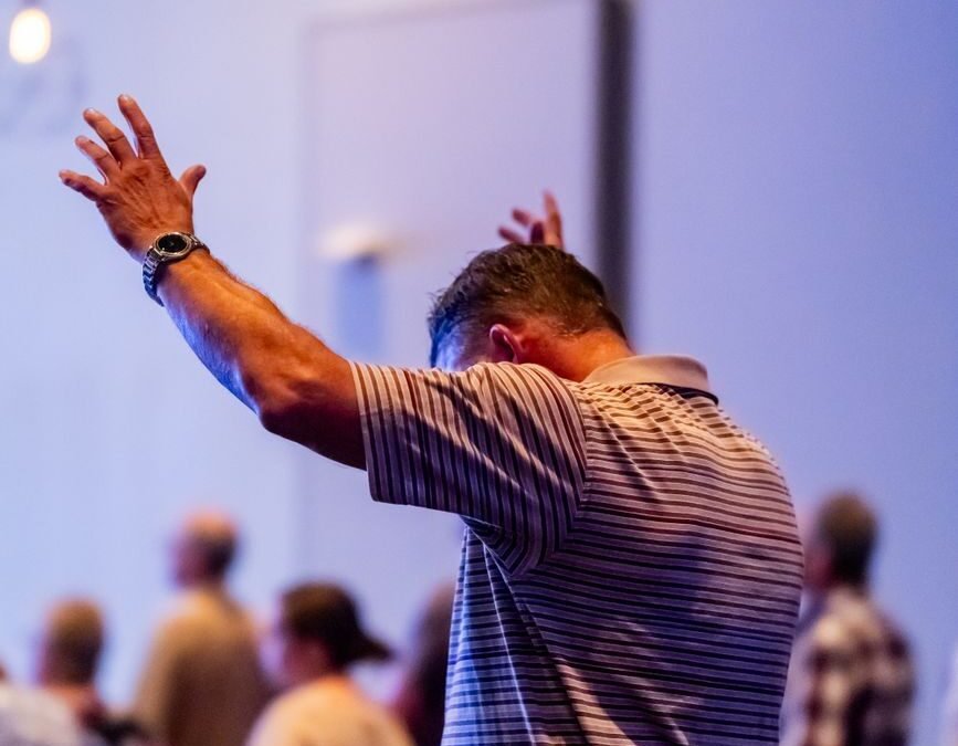 man raising arms in worship at church service